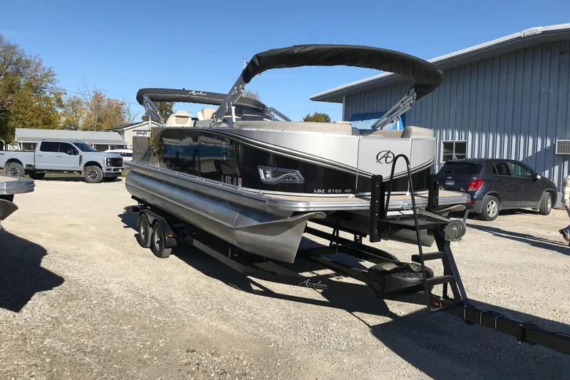 The Image of 2023 Avalon LSZ Rear Fish pontoon boat on trailer, parked outdoors. - 0