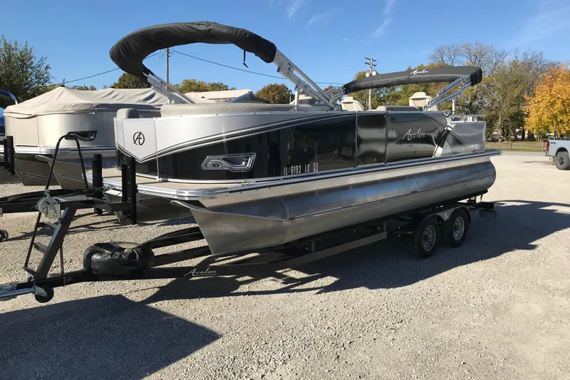 Slide: The Image of 2023 Avalon LSZ Rear Fish pontoon boat on trailer, parked outdoors. - 2