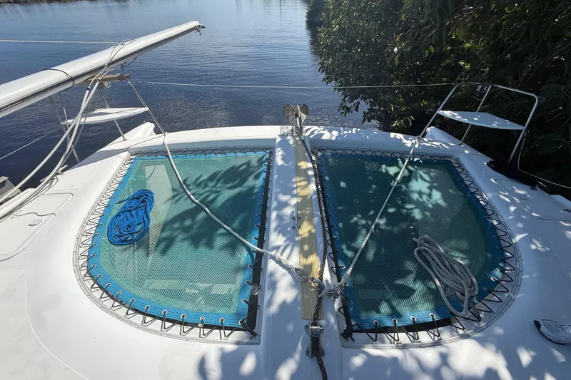 Slide: The Image of 1995 Manta SAILING CATAMARAN with dual trampolines and ropes, docked by lush greenery. - 7