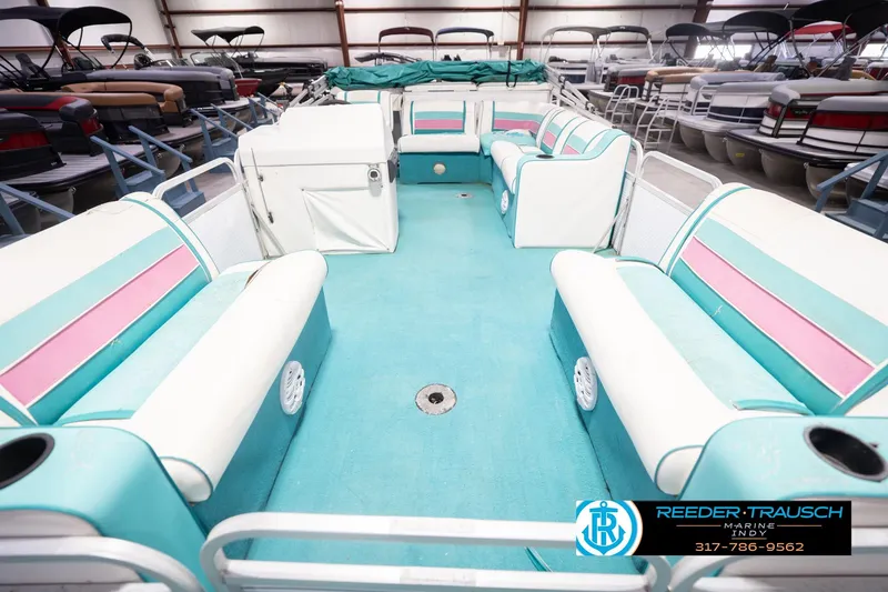 Slide: The Image of 1993 Avalon Playbouy Challenger pontoon boat interior with teal and pink seating in a showroom. - 15