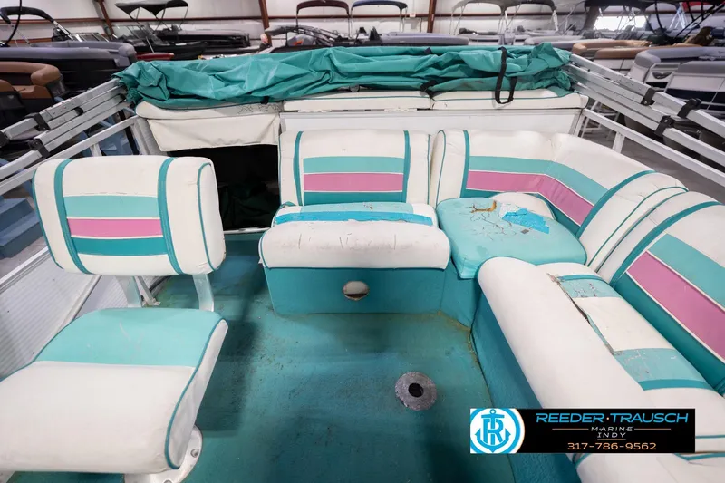 Slide: The Image of 1993 Avalon Playbouy Challenger boat interior with teal and pink seating, showing wear and tear. - 17