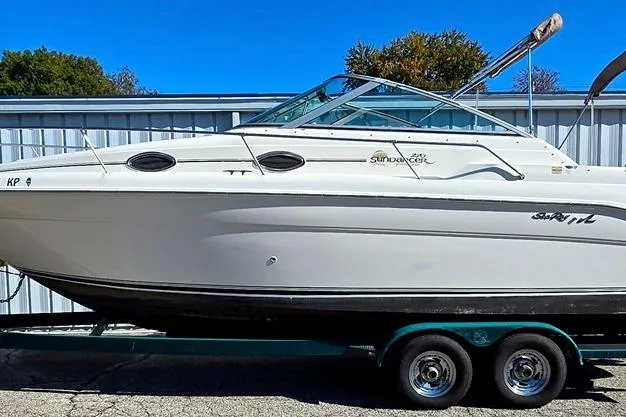 The Image of 1999 Sea Ray 270 Sundancer boat on trailer, parked outdoors near a metal building. - 0