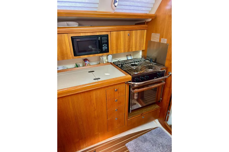 Slide: The Image of Compact kitchen in a 2004 Hunter 386 sailboat with stove, microwave, and wooden cabinetry. - 6