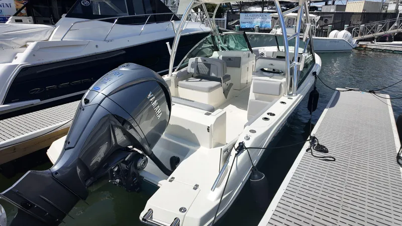 Slide: The Image of 2025 Cobia 240 Dual Console boat docked in a marina, under a partly cloudy sky. - 1