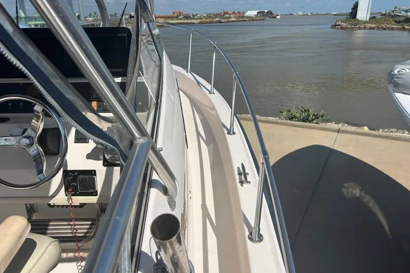 Slide: The Image of 2004 Grady-White Marlin 300 boat docked by a calm river, featuring steering wheel and controls. - 26