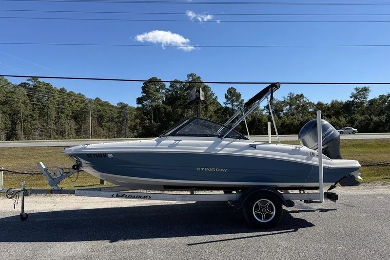 The Image of 2024 Stingray 191 DC boat on trailer, parked roadside under clear blue sky. - 0