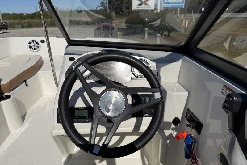 Slide: The Image of 2024 Stingray 191 DC boat interior with seating and steering wheel, parked outdoors. - 10