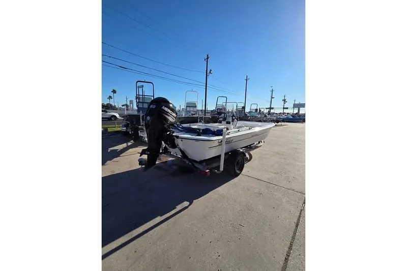 Slide: The Image of 2018 Mako Pro Skiff 17 CC boat on trailer, parked outdoors under clear blue sky. - 2