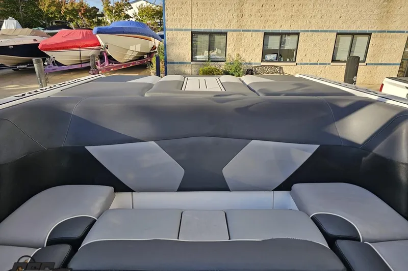 Slide: The Image of 2020 Moomba Max boat interior with gray and black seating, parked near other covered boats. - 86