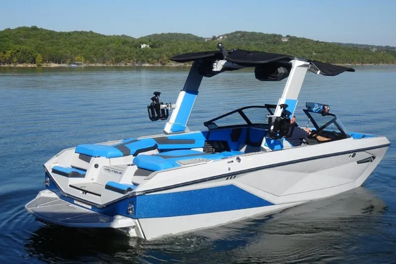 Slide: The Image of 2024 Nautique Super Air Nautique G23 boat on a serene lake with lush green hills. - 10
