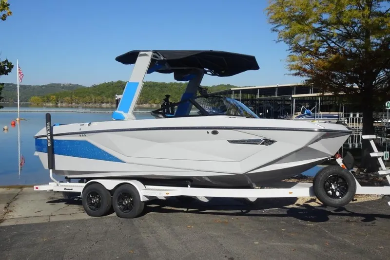 Slide: The Image of 2024 Nautique Super Air Nautique G23 boat on trailer by a lake. - 2