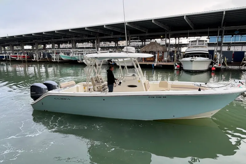 Slide: The Image of 2017 Cobia 296 Center Console boat docked in marina with dual Yamaha engines. - 12