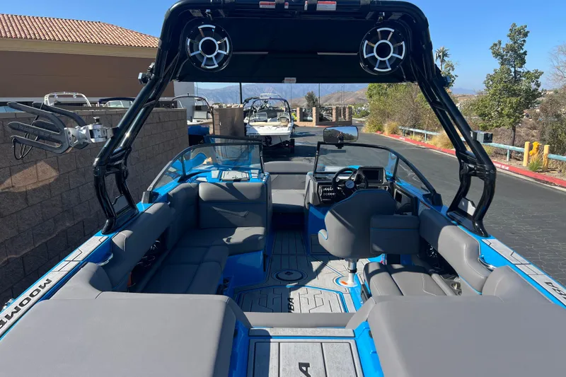 Slide: The Image of 2022 Moomba Kaiyen boat interior with gray seating and blue accents, parked outdoors. - 14