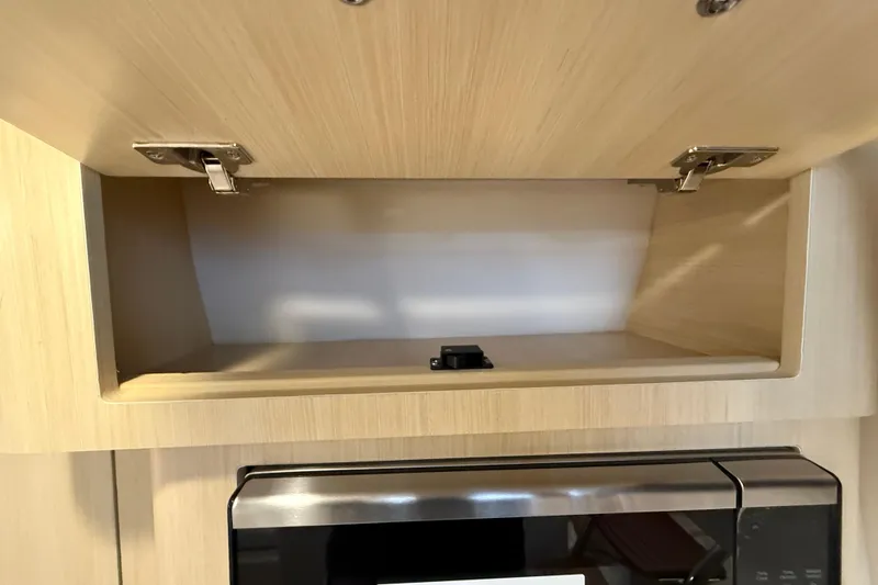Slide: The Image of Open wooden cabinet above a microwave in a 2026 Regal 28 Express boat. - 43