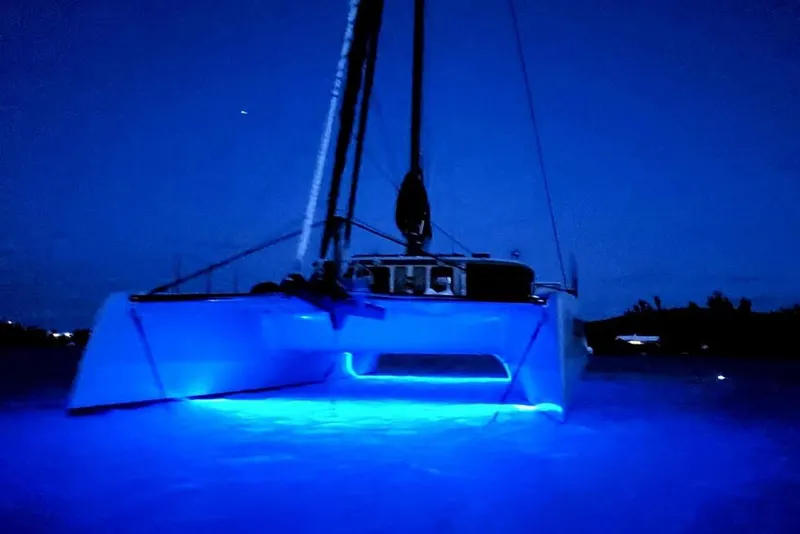Slide: The Image of Illuminated Harvey Yachts 58 catamaran, 2017 model, glowing blue on water at night. - 111