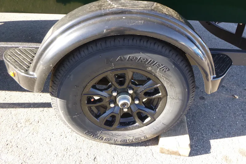 Slide: The Image of 2026 Tracker Bass Tracker Classic Limited trailer wheel on pavement, featuring black fender and Karrier tire. - 6