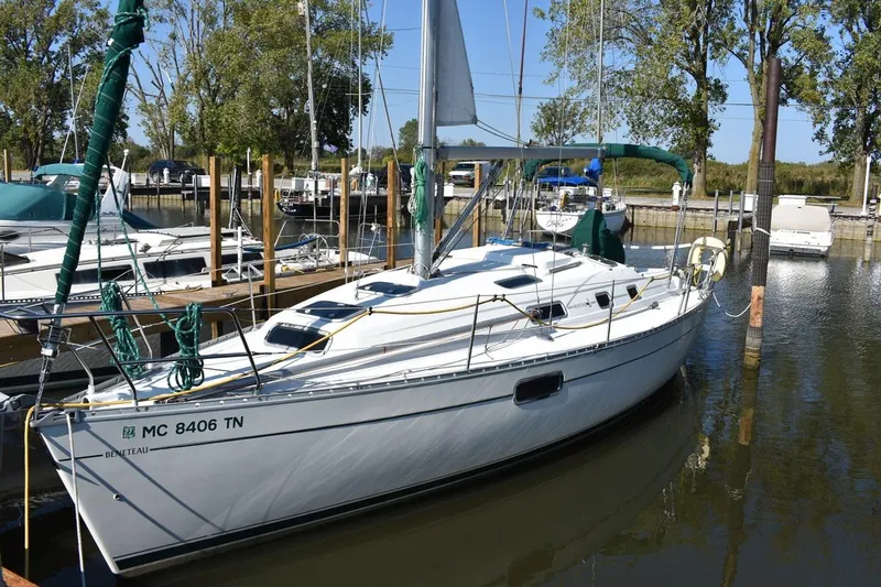 The Image of 1996 Beneteau Oceanis 321 sailboat docked in a marina, surrounded by trees and other boats. - 0